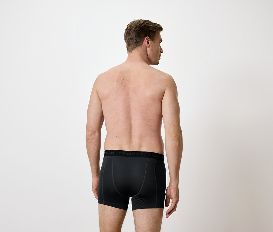 Beyaz bir arka plan üzerinde siyah boxer şortlu bir adamın arka görünümü.