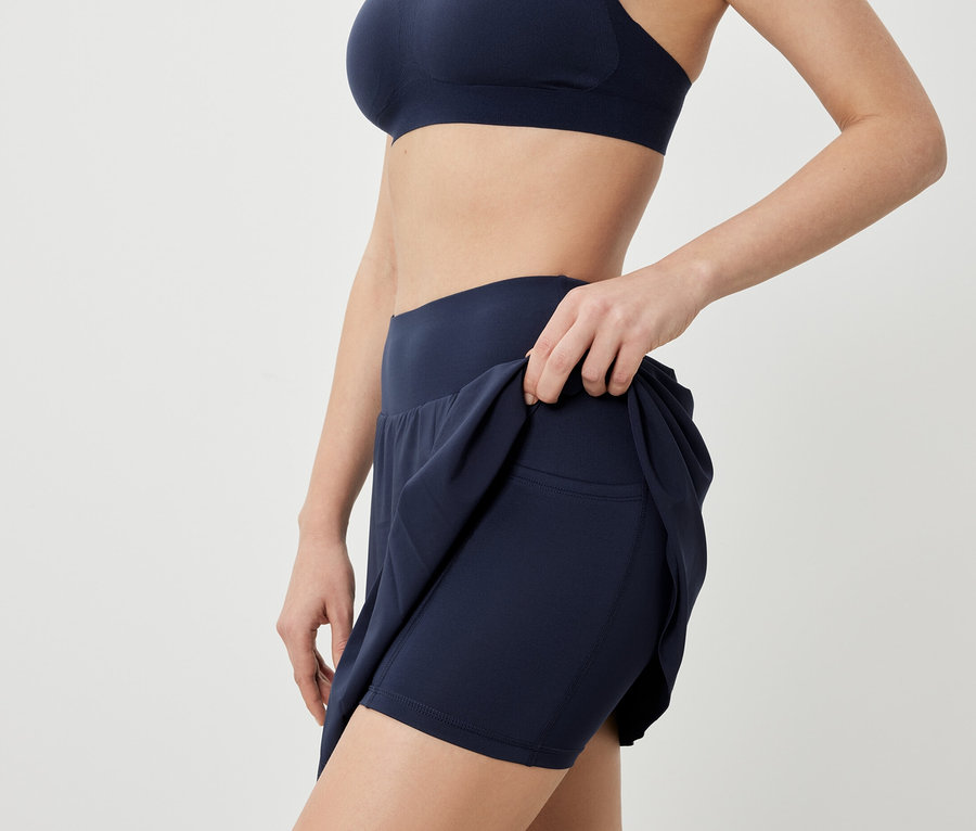 Kadın spor sütyeni ve lacivert spor etekle poz veriyor.