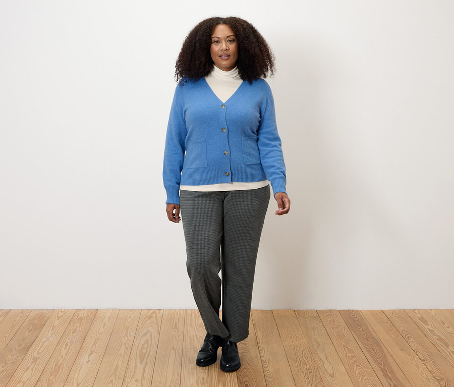 Kadın krem beyaz balıkçı yaka tişört, mavi hırka ve gri pantolon giyiyor.