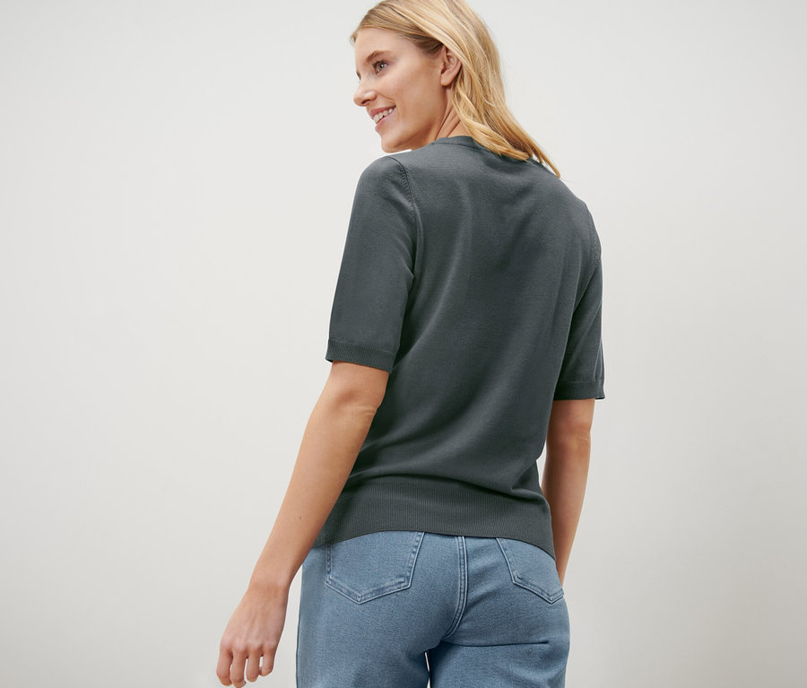 Omzunun üzerinden bakan bir kadın, üzerinde yeşil ince triko bir kazak ve kot pantolon var.