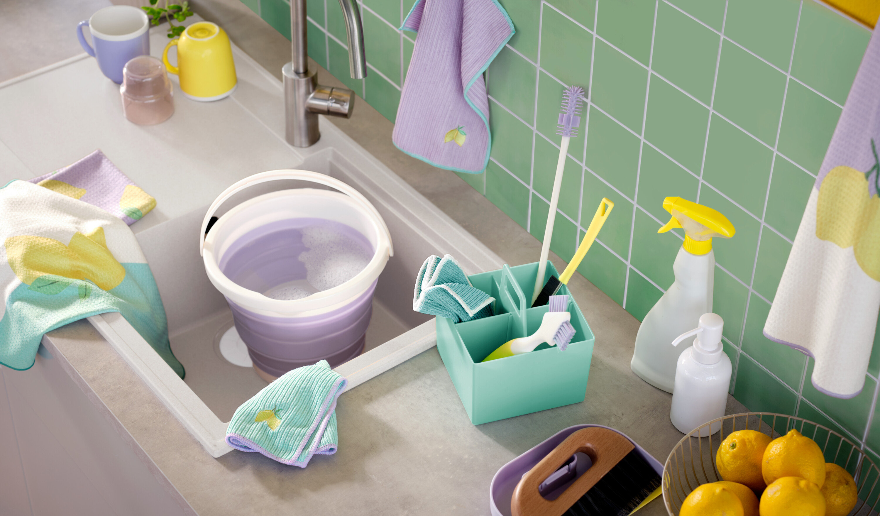 Lavaboda sabunlu su bulunan mor bir kova, etrafında fırçalar, spreyler ve bezler gibi temizlik malzemeleri bulunmaktadır.