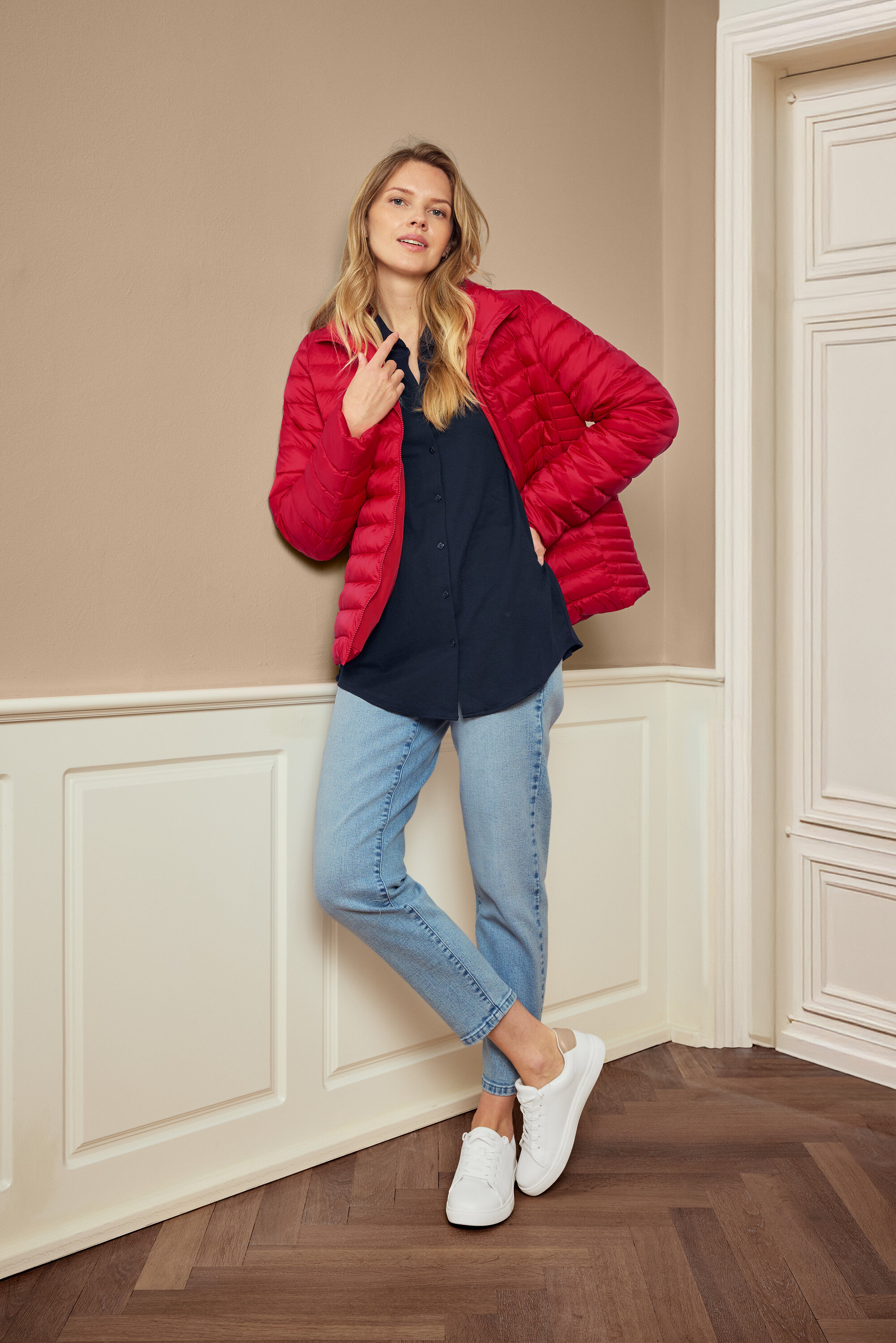 Kadın kırmızı ceket, mavi gömlek, kot pantolon ve beyaz spor ayakkabılarıyla poz veriyor, 925 gümüş halka küpe Hexagon takıyor.