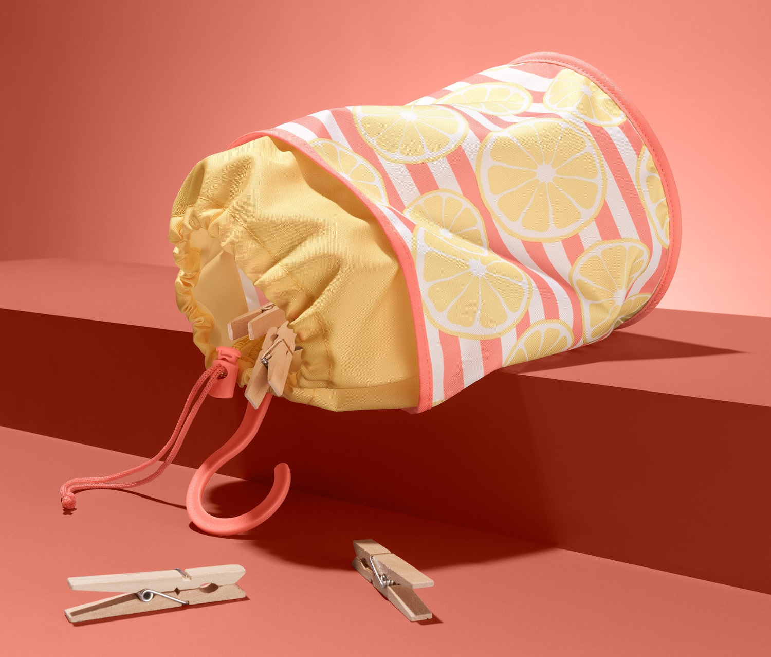 Mandal torbası, mercan rengi bir platformun üzerinde duruyor, yanında iki adet mandal var.