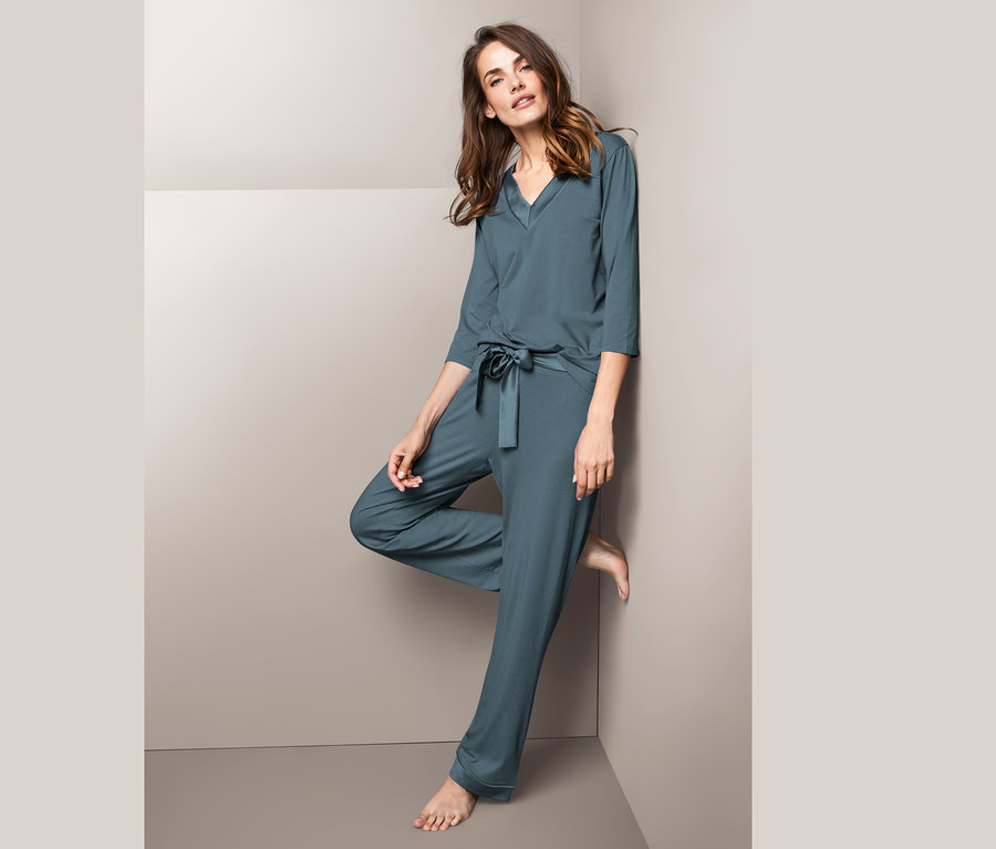 Duvara yaslanmış, saten pijama takımı giyen kadın.