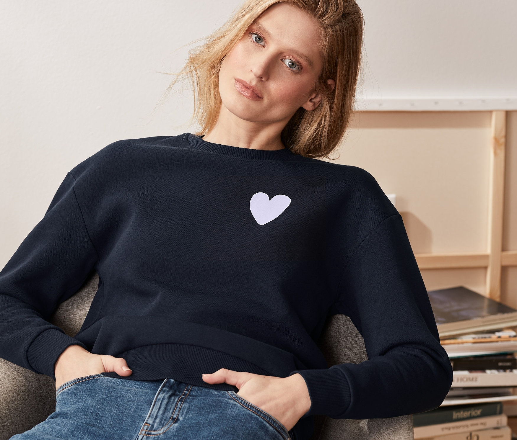 Bir kadın koltukta oturuyor ve lacivert bir sweatshirt giyiyor.