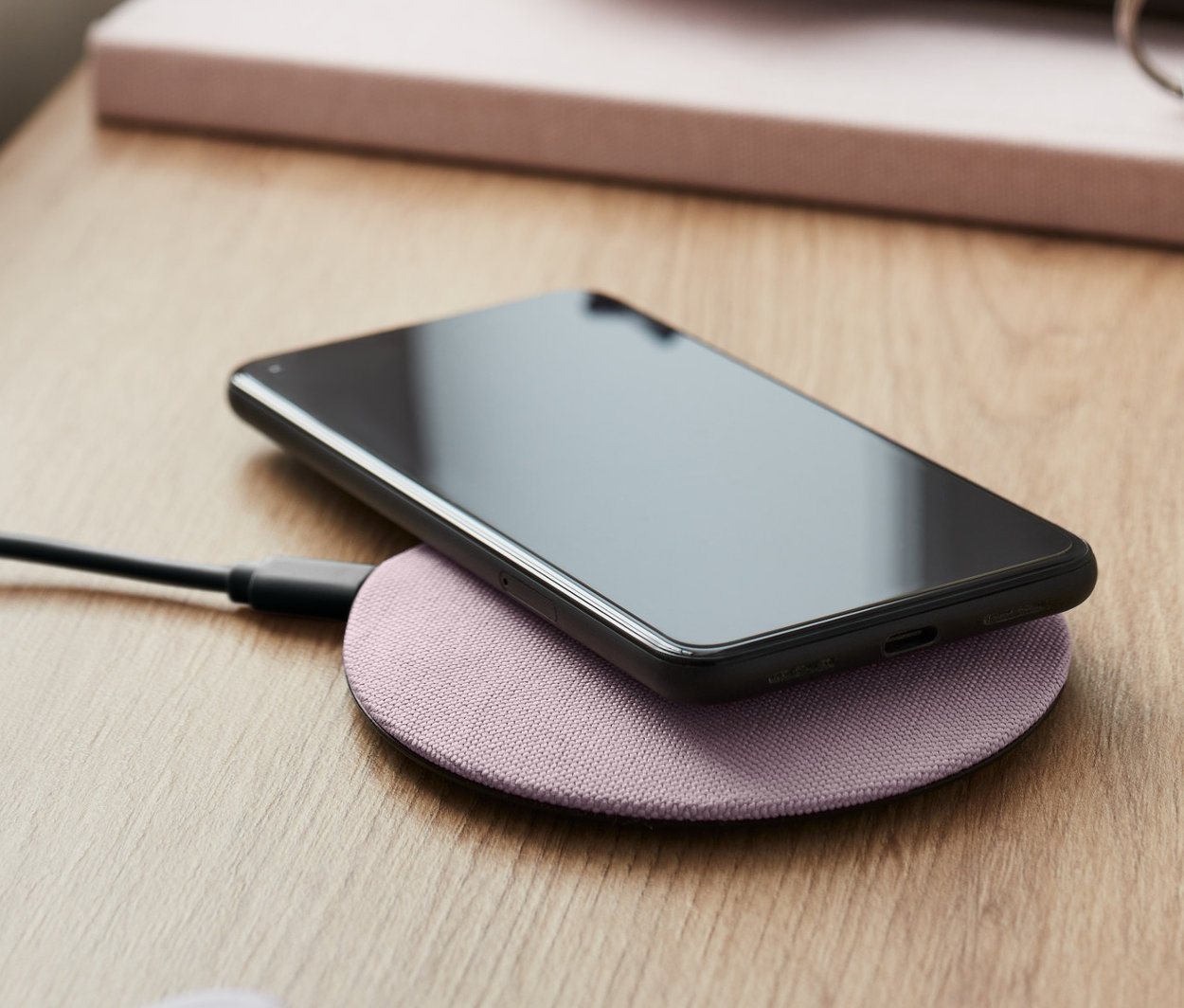 Siyah akıllı telefon, pembe kablosuz şarj istasyonunda şarj oluyor.