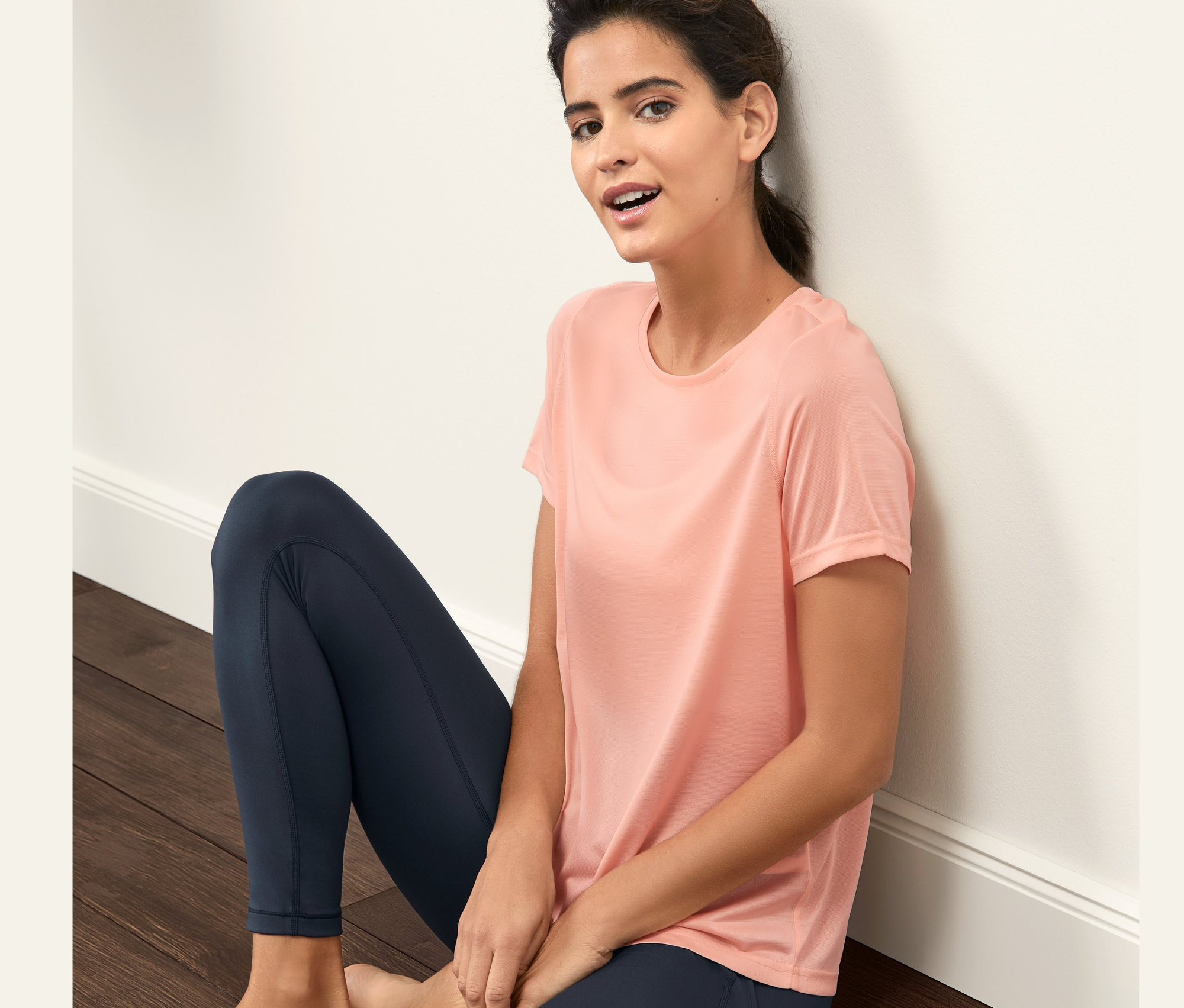 Kadın yerde oturuyor, üzerinde Mercan Rengi Spor Tişörtü var.