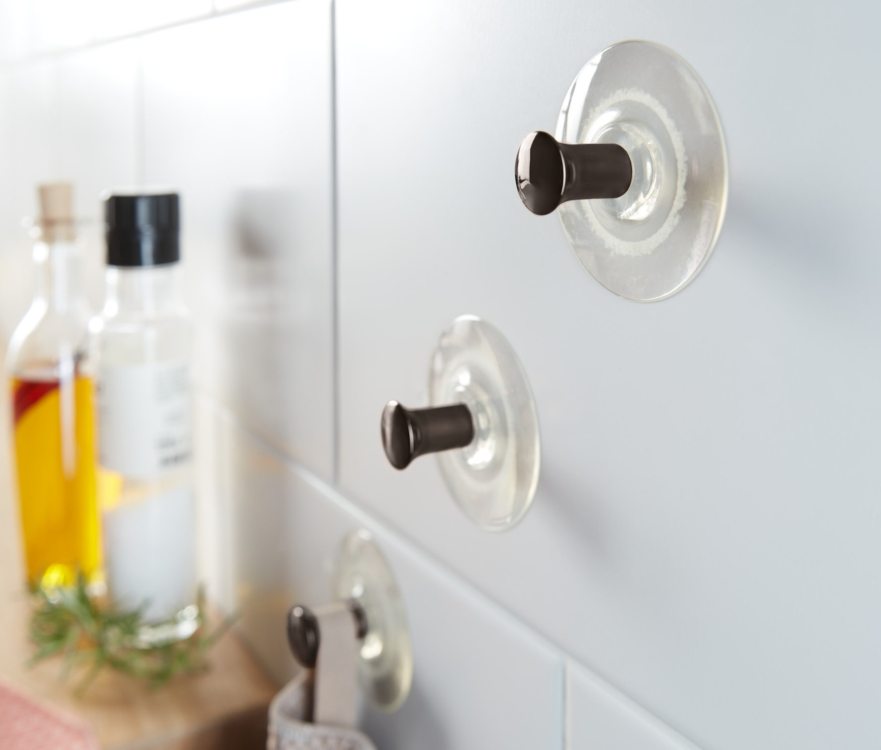 Beyaz fayanslara tutturulmuş 3 adet vantuzlu kanca, bir kancada asılı gri havlu.