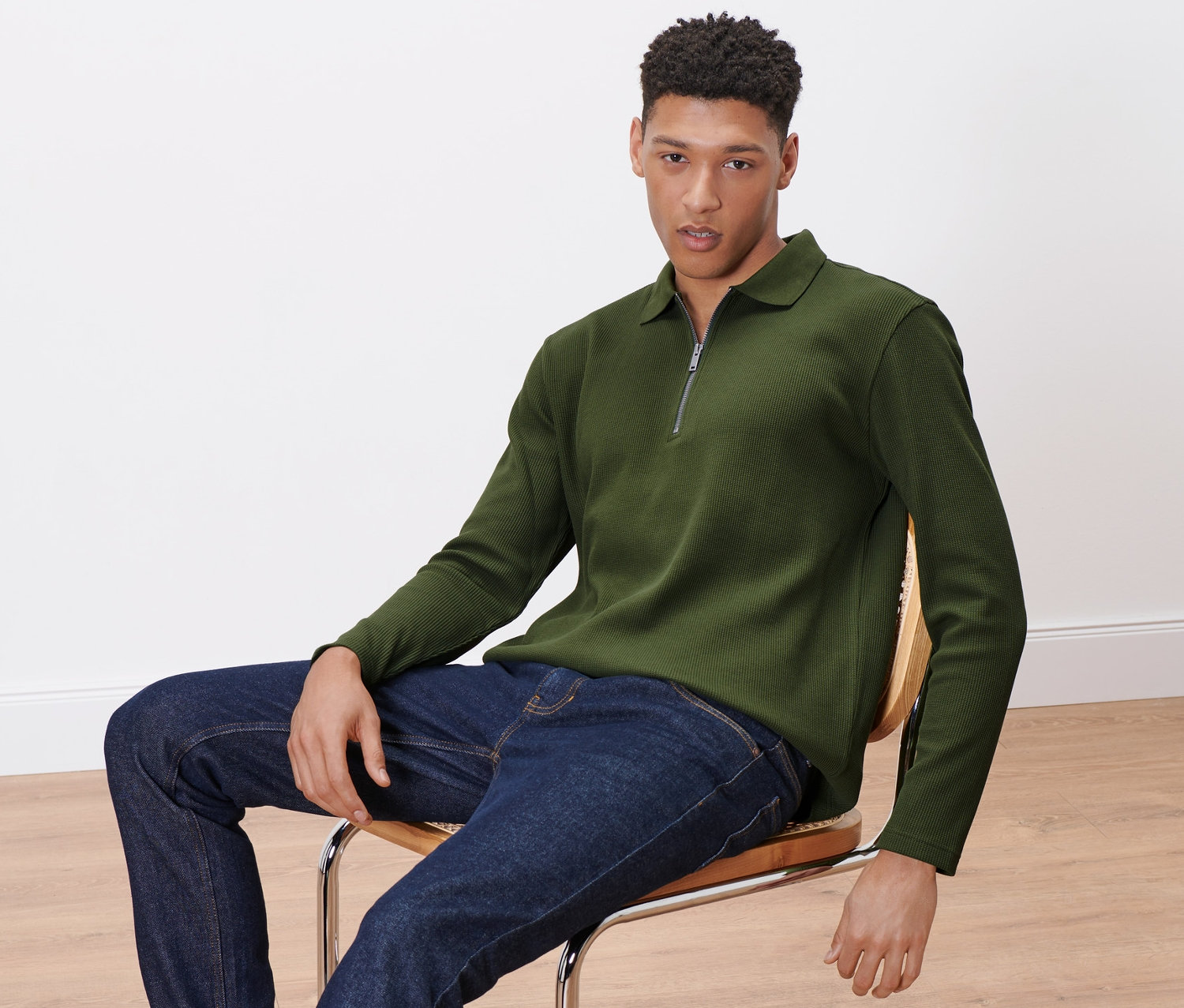 Adam sandalyede oturuyor, üzerinde Uzun Kollu Polo Üst var.