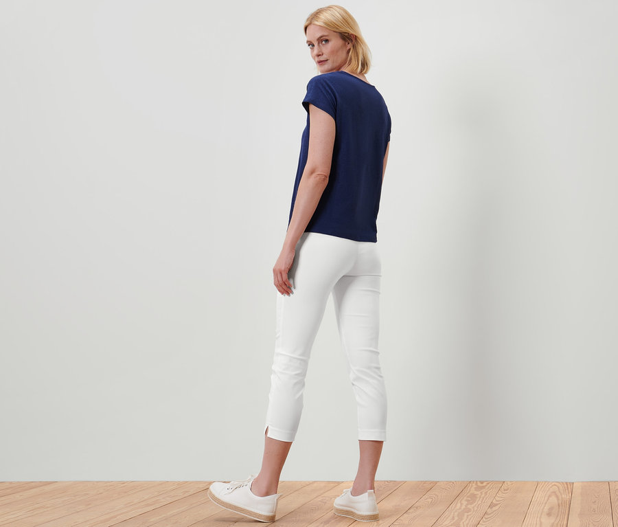 Bir kadın kameraya arkası dönük duruyor, beyaz 7/8 streç pantolon ve lacivert tişört giyiyor.