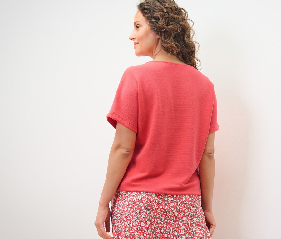 Omuzunun üzerinden bakan kadın, mercan rengi bir bluz giyiyor.