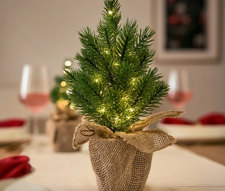 Şenlikli bir masada jüt saksıda ışıklarla küçük bir Noel ağacı.
