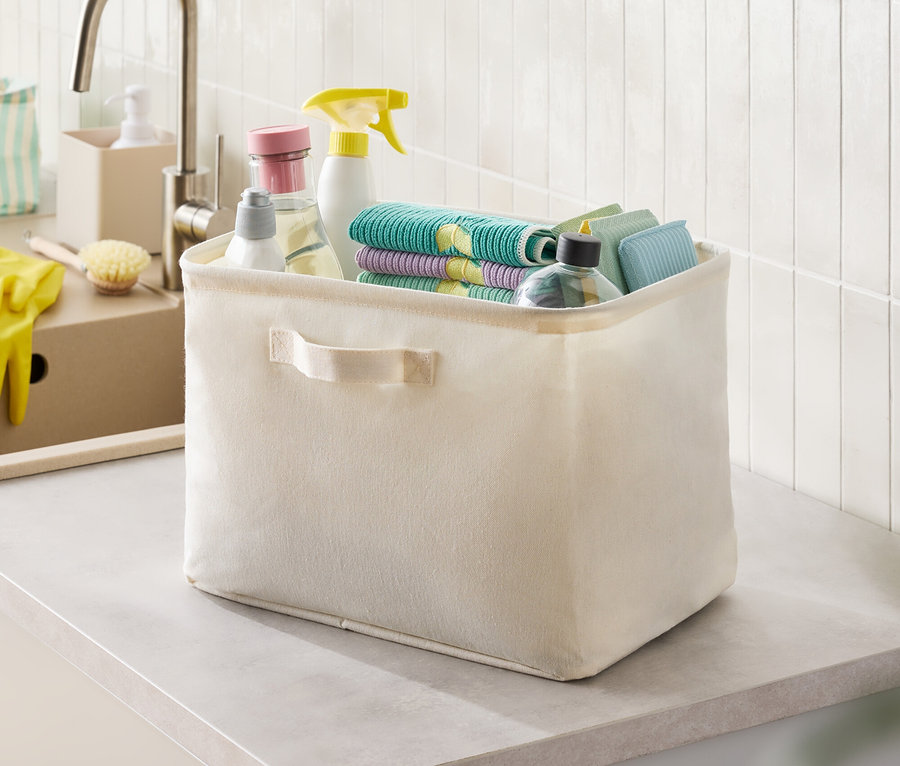 Tezgah üzerinde temizlik malzemeleri ve bezlerle dolu bej kumaş kutu.