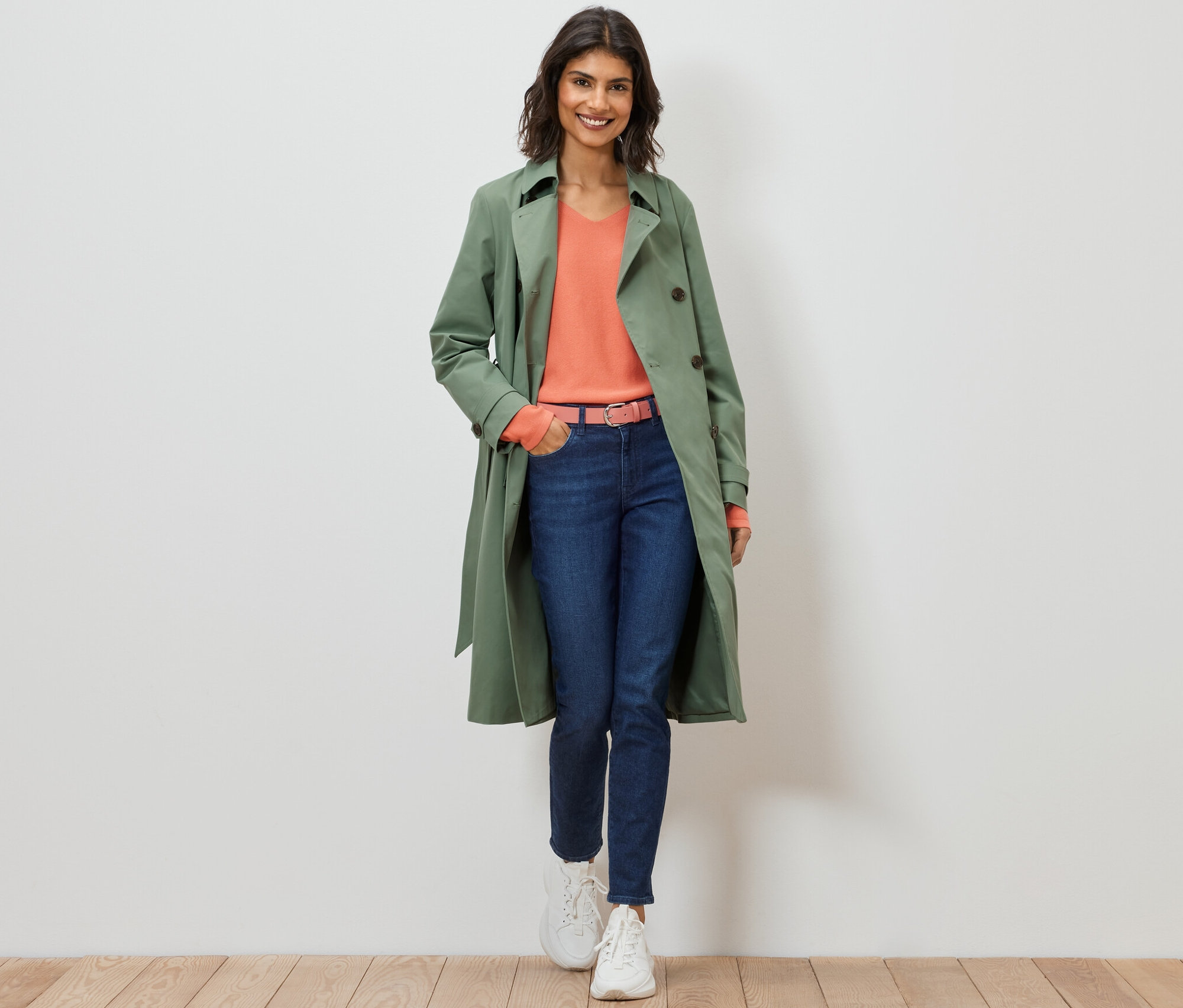 Kadın yürüyor ve açık yeşil bir trençkot giyiyor.