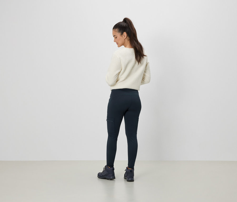 Krem rengi bir kazak ve cepli lacivert tayt giyen bir kadın arkadan görülüyor.