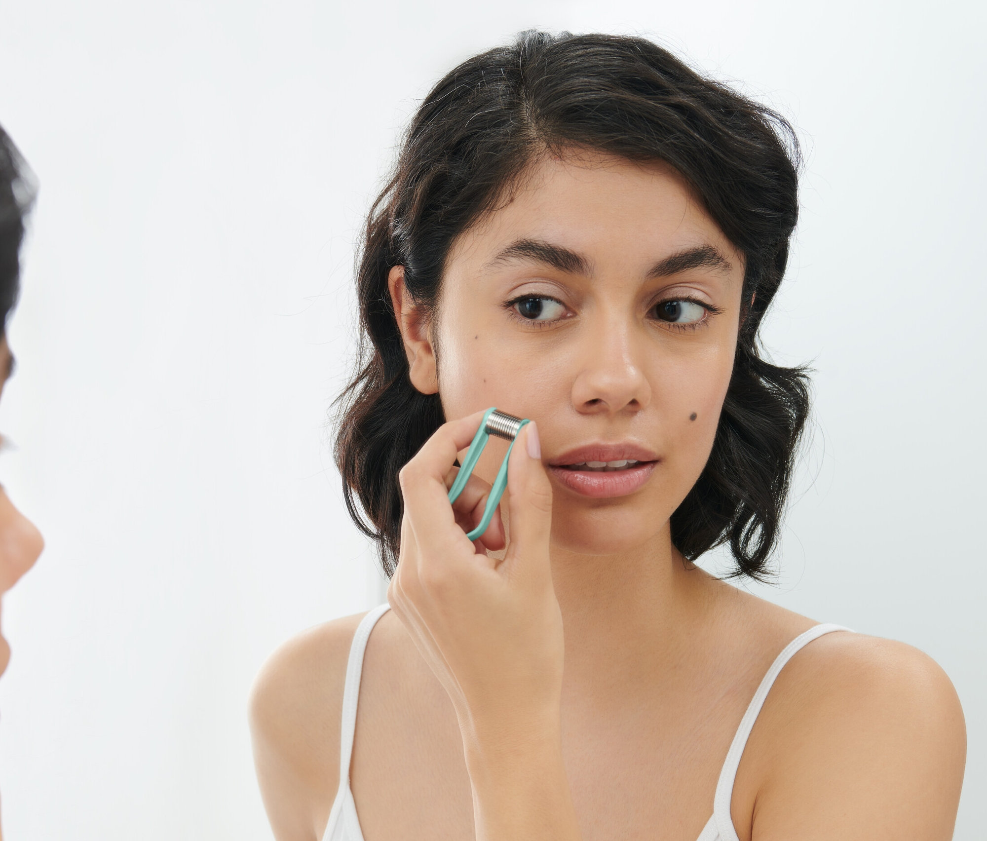 Kadın aynanın önünde yüzünde mikro iğneli silindir kullanıyor.