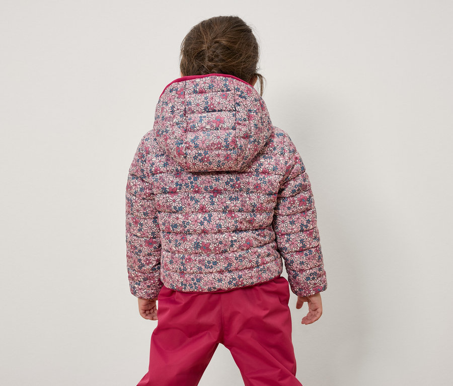 Kameraya arkası dönük bir kız çocuğu çiçekli bir ceket ve pembe bir pantolon giyiyor.