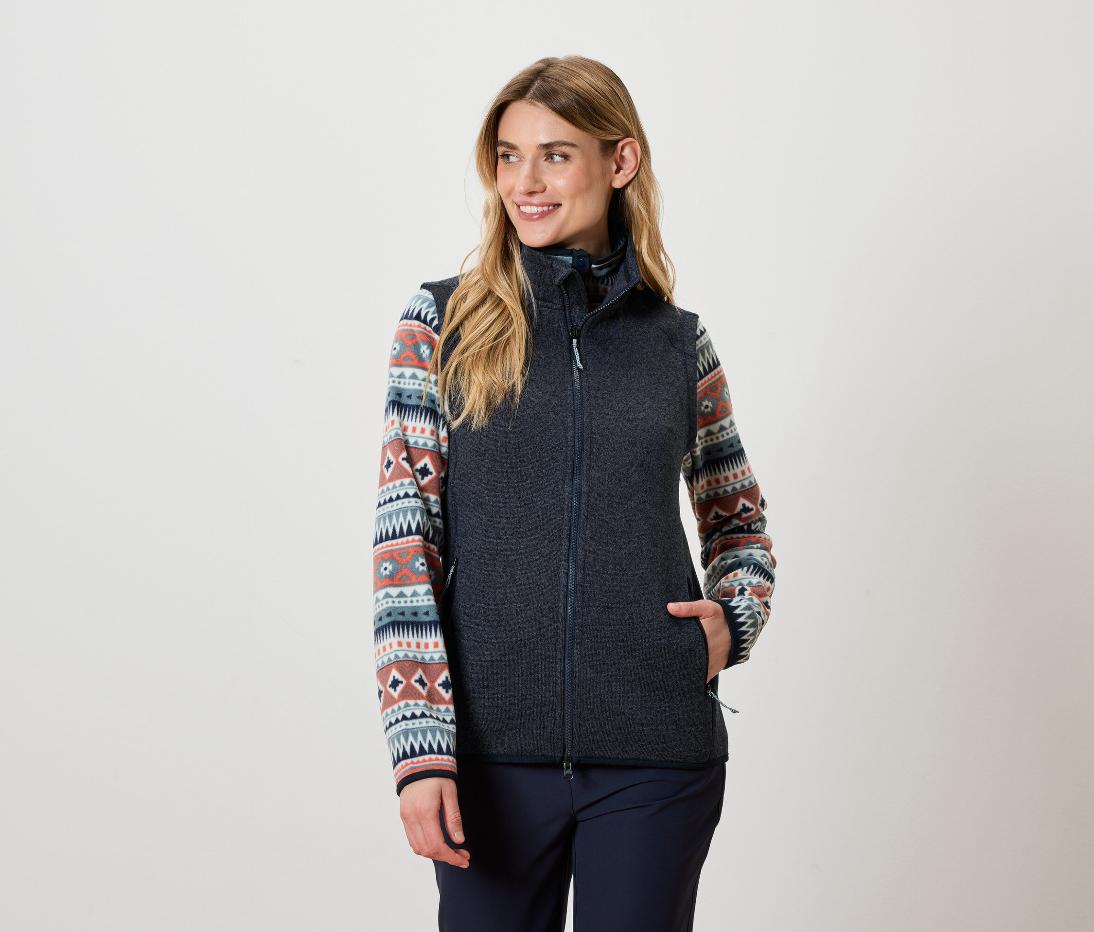Kadın koyu gri bir yelek ve desenli bir üst giyiyor.