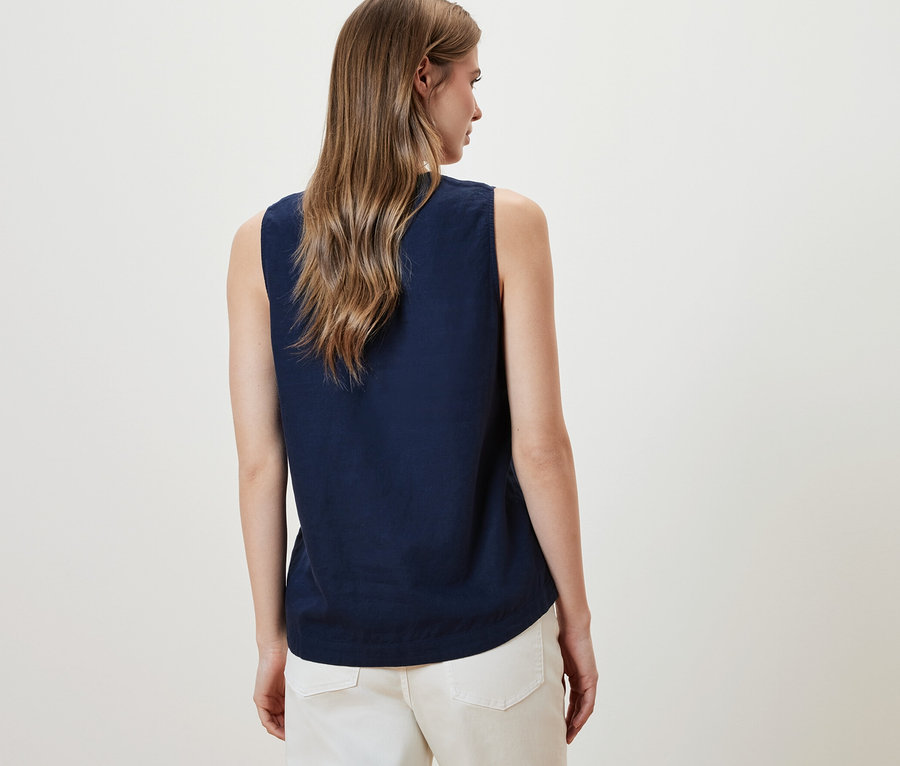 Kadın lacivert kolsuz keten bluz ve beyaz pantolon giyiyor.