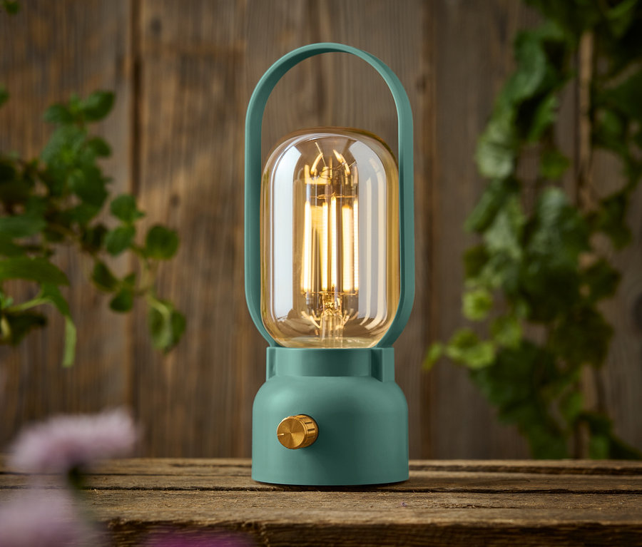 Ahşap bir masanın üzerinde altın düğmeli yeşil bir lamba duruyor.