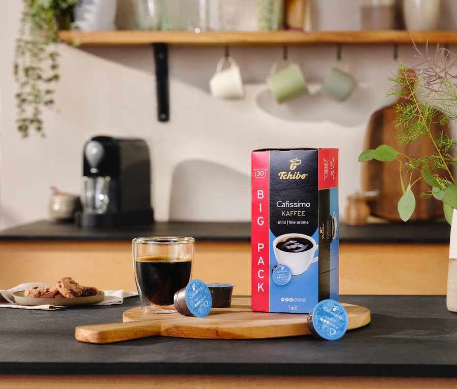 Tezgahta bir bardak kahve, bir paket Cafissimo Pure+, Siyah ve iki kapsül duruyor.