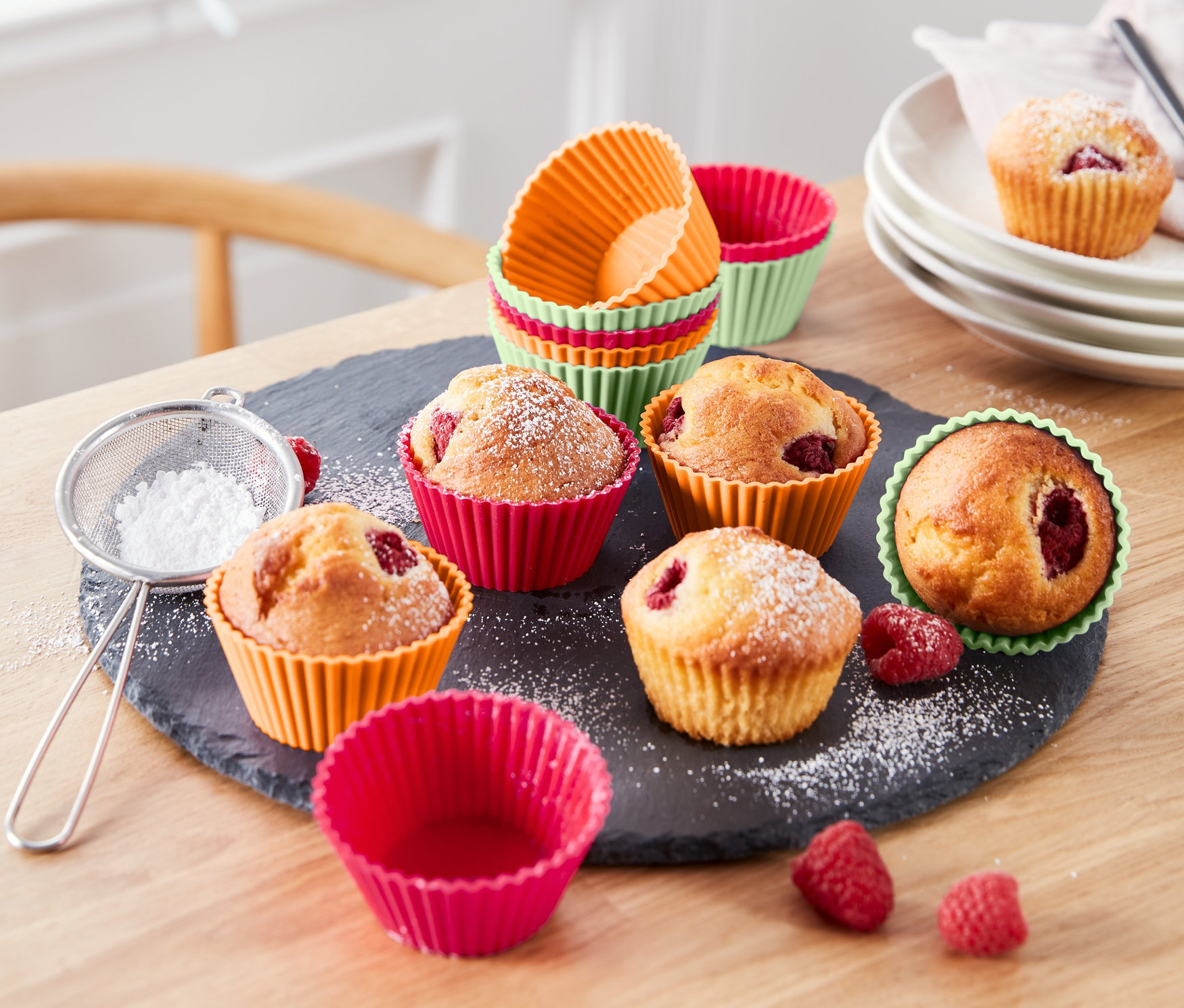 Bir masa üzerinde pudra şekeri serpilmiş renkli 12 Adet Muffin Kalıbı içinde muffinler bulunmaktadır.