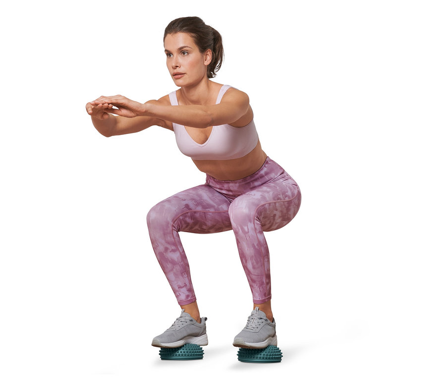 Bir kadın 2 adet denge ve masaj pedi üzerinde çömeliyor.