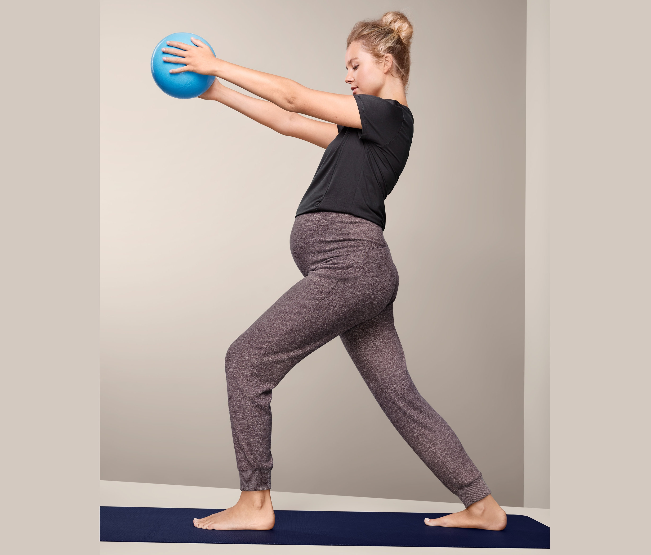 Hamile bir kadın mat üzerinde mavi bir topla egzersiz yapıyor ve Hamile Eşofman Altı giyiyor.