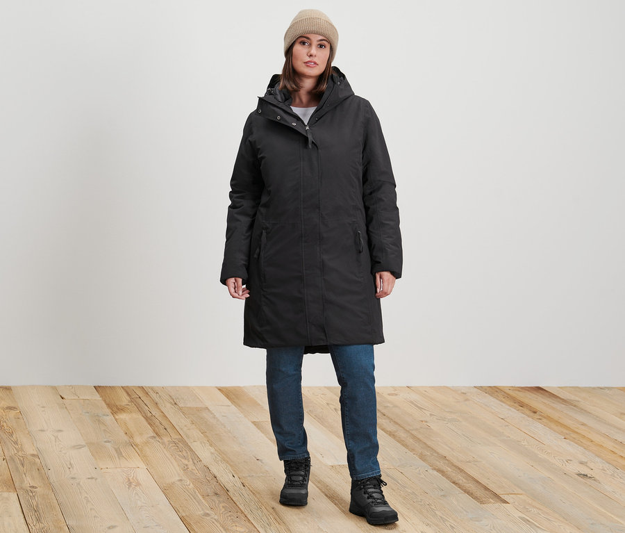 Kadın, siyah termal mont, koyu mavi slim fit Emma kot pantolon ve ekru örgü bere giyiyor.