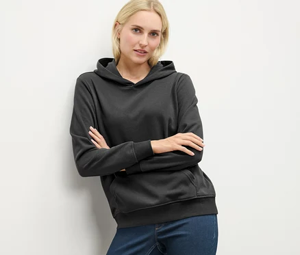 Sarışın bir kadın antrasit rengi kapüşonlu bir sweatshirt ile poz veriyor.