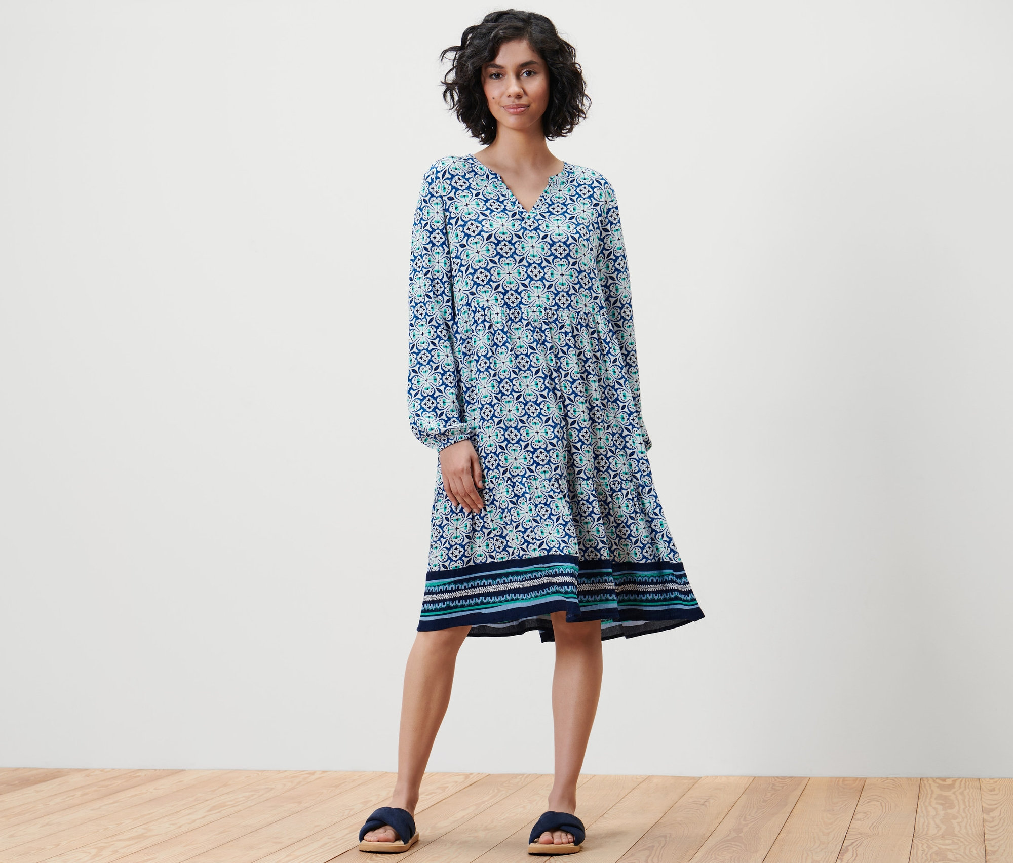 Kadın ayakta duruyor ve tamamı baskılı dokuma bir elbise giyiyor.