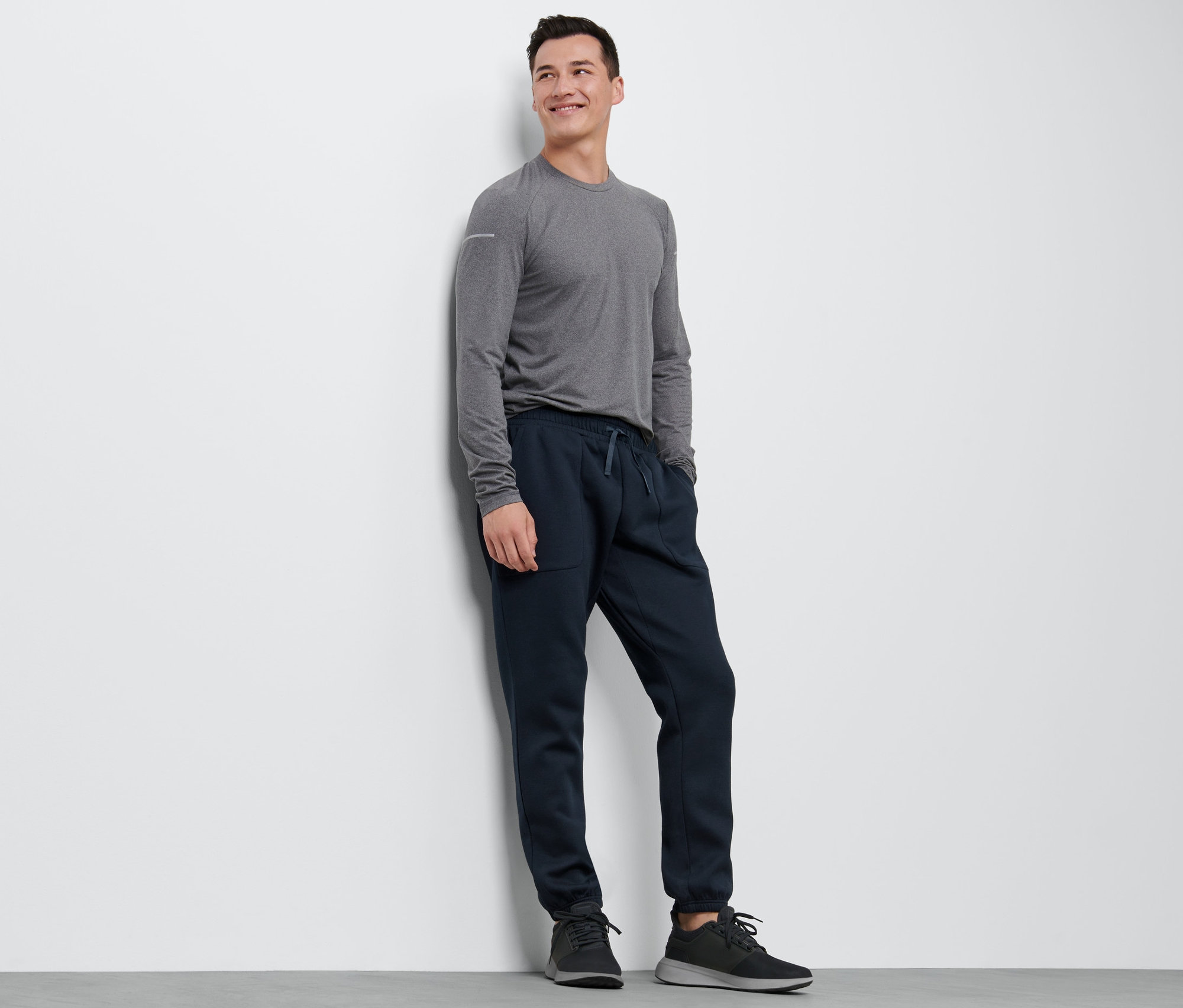 Gri tişörtü ve eşofman altı olan bir adam duvara yaslanmış.