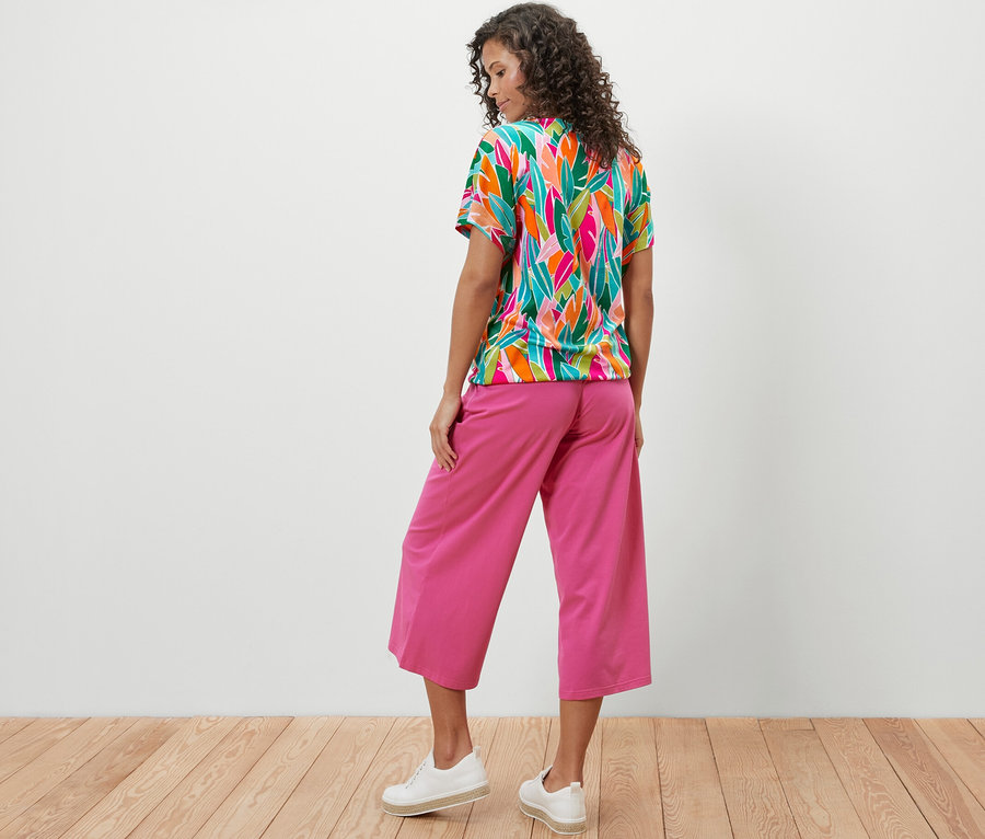 Kadın arkadan düşük omuzlu, tamamı baskılı tişört ve pembe pantolon giyiyor.