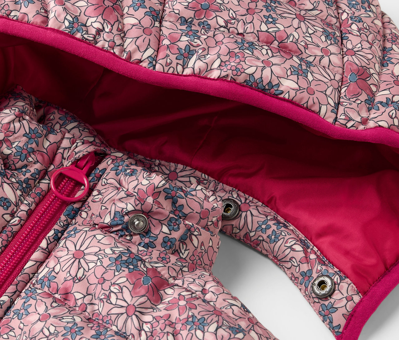 Çiçek desenli çocuk şişme montunun, fermuar ve çıtçıt detayının yakın çekimi.