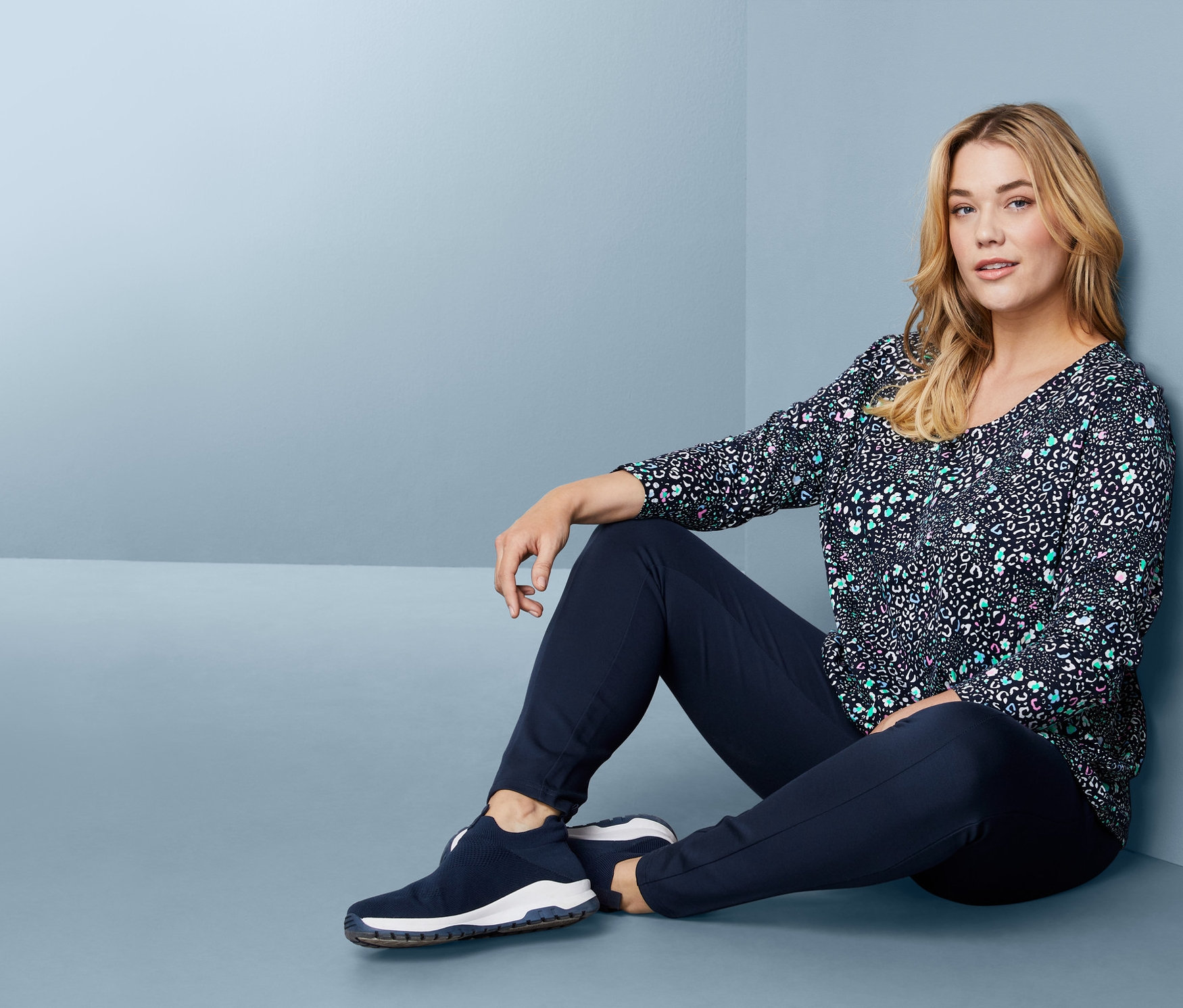 Kadın yerde oturuyor, üzerinde Uzun Kollu Tişört, altında Bağcıksız Sneaker var.