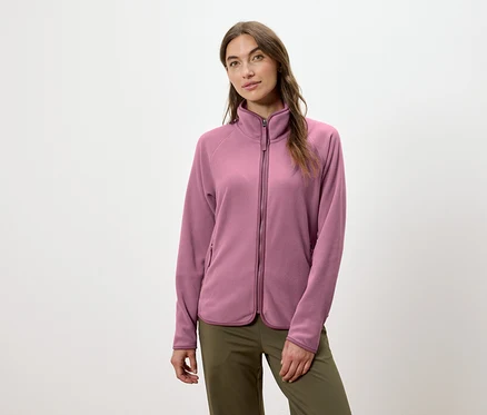 Bir kadın pembe fermuarlı polar ceket ve yeşil pantolon giyiyor.