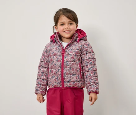 Çiçekli ceket ve pembe pantolon giyen bir kız çocuğu.
