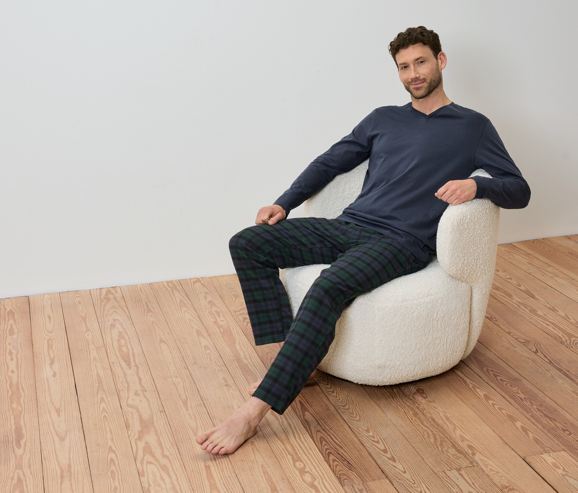 Adam, mavi uzun kollu tişörtü ve ekose pantolonuyla bir koltukta oturuyor.