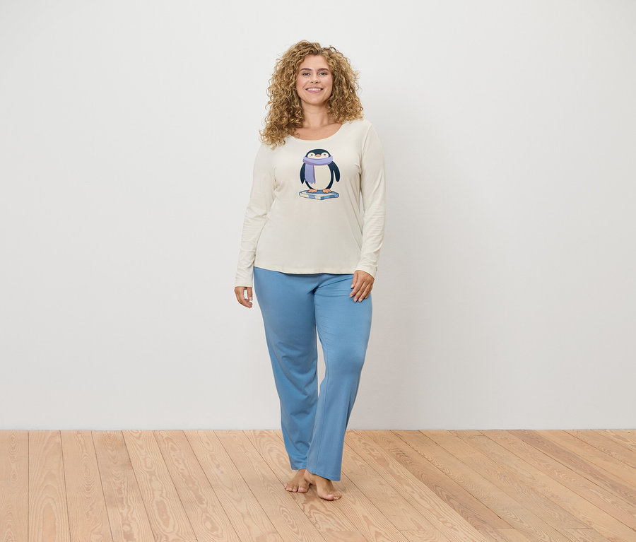 Kadın penguen baskılı krem rengi bir pijama üstü ve mavi bir pijama altı ile poz veriyor.