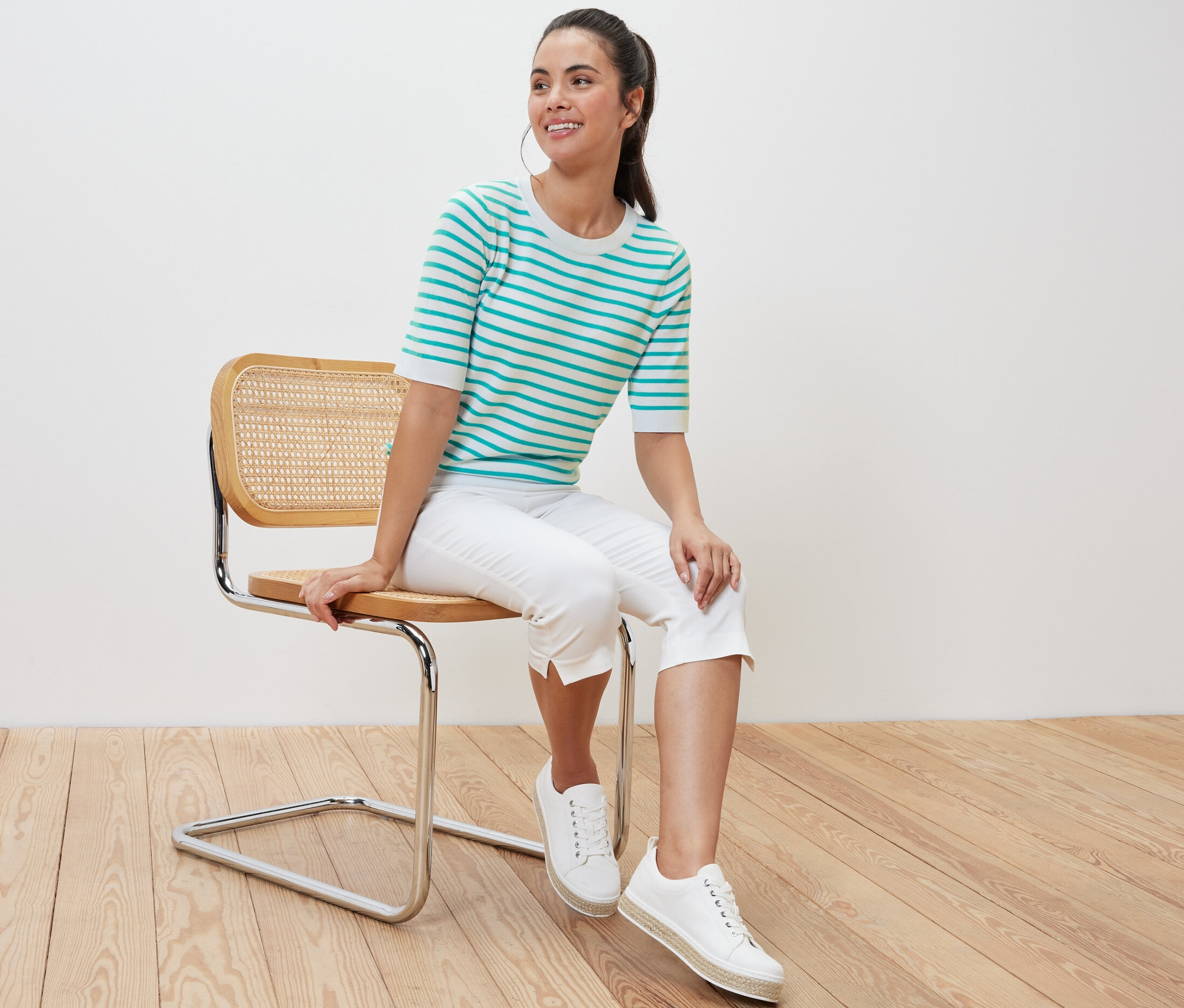 Kadın sandalyede oturuyor ve Deniz Mavisi Çizgili İnce Örgülü Kazak giyiyor.