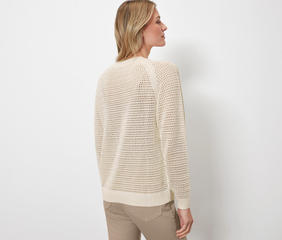 Yan duran bir kadın pointelle örgü bir kazak ve pantolon giyiyor.