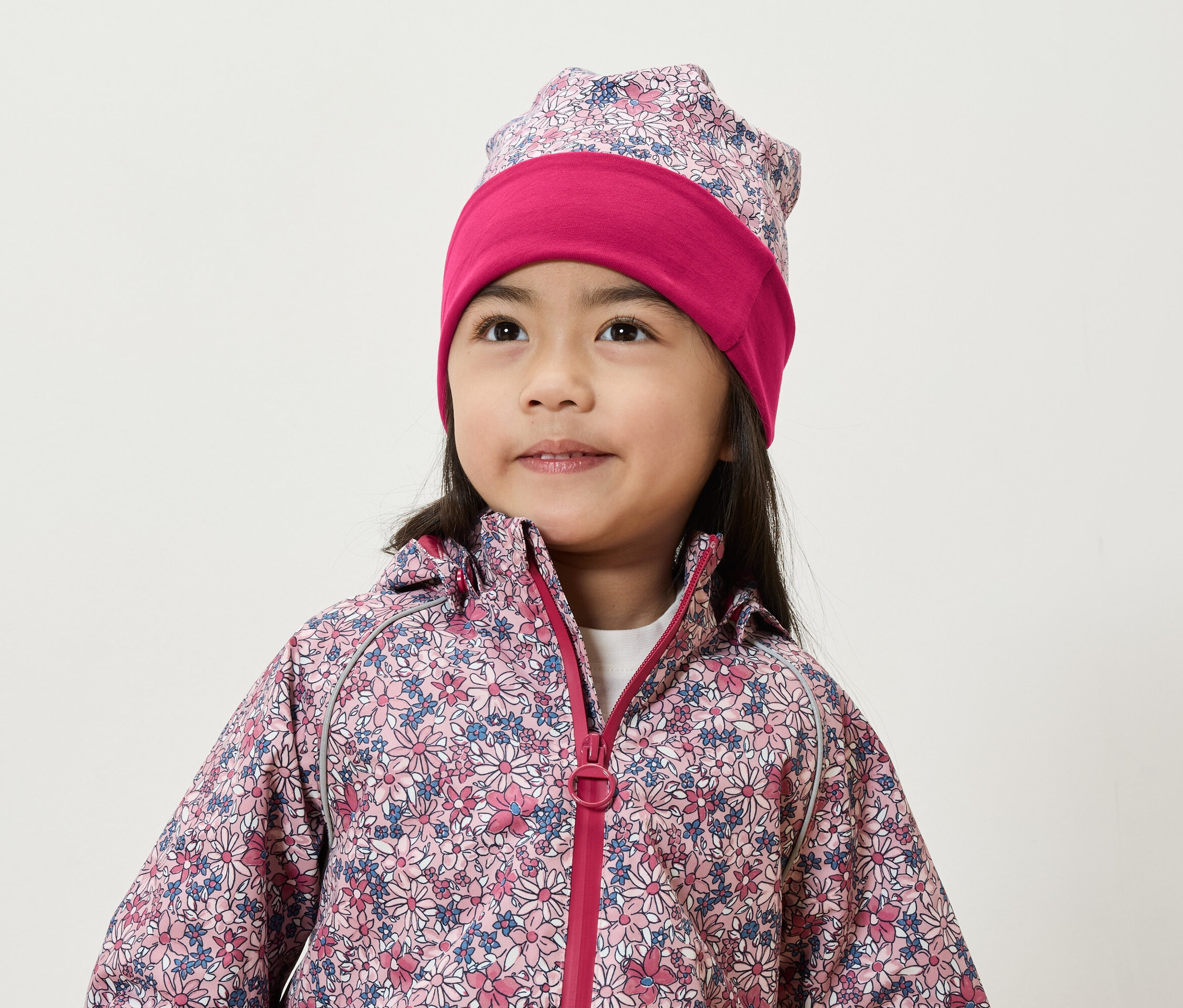 Gülümseyen bir kız, çiçekli bir ceket ve şapka giyiyor.