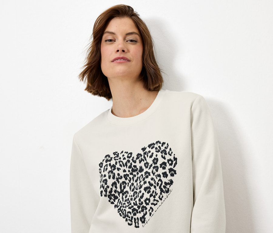 Kadın leopar desenli kalbi olan krem rengi bir sweatshirt giyiyor.
