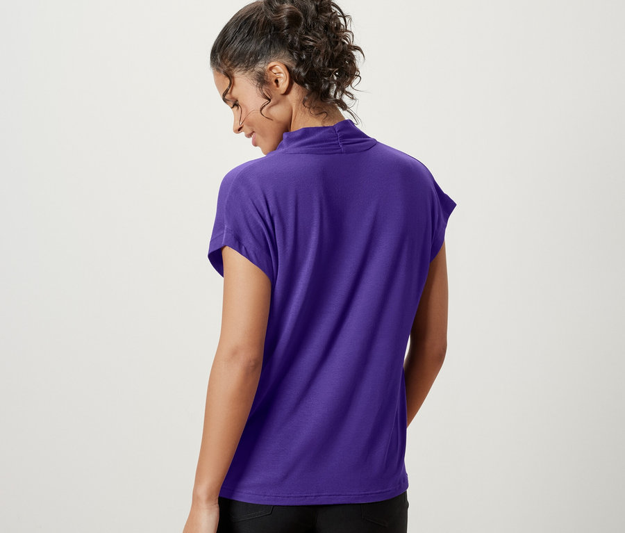 Arkası dönük bir kadın, mor V yakalı bluz ve siyah şort giyiyor.