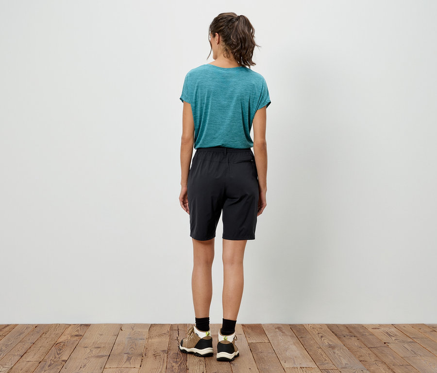 Atkuyruklu, deniz mavisi tişört, siyah şort ve tahta zeminde spor ayakkabı giyen bir kadının arka görünümü.