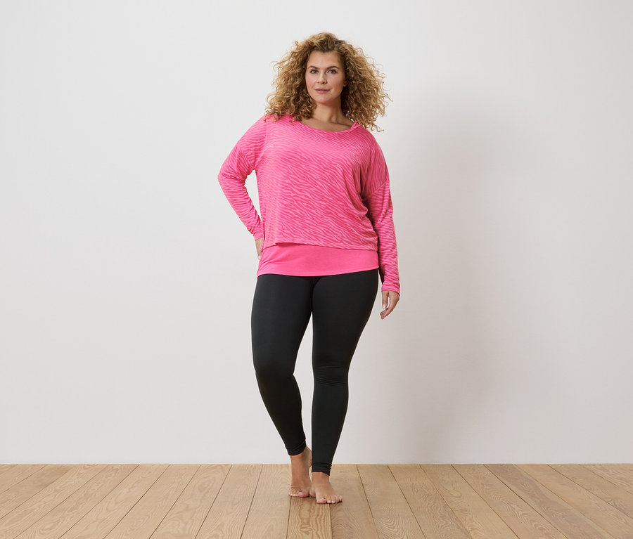 Kıvırcık saçlı bir kadın pembe zebra uzun kollu tişört ve siyah tayt giyiyor.