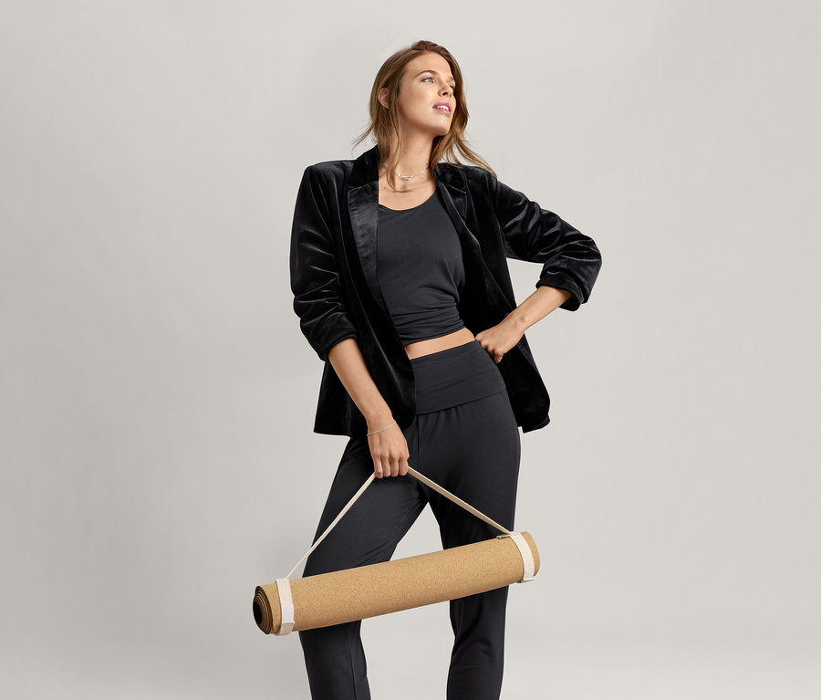 Kadın siyah 2'si 1 Arada Kadın Spor Tişörtü giyiyor ve bir yoga matı tutuyor.