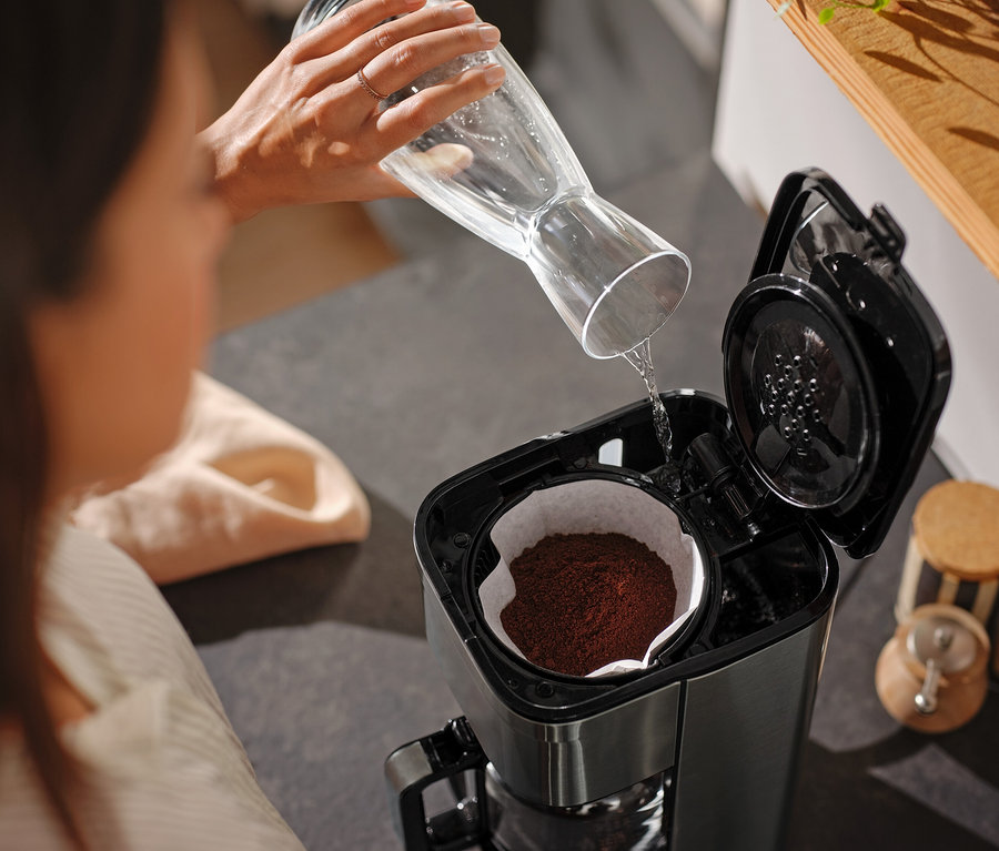 Kadın, cam bir sürahiden kahve makinesine su döküyor.