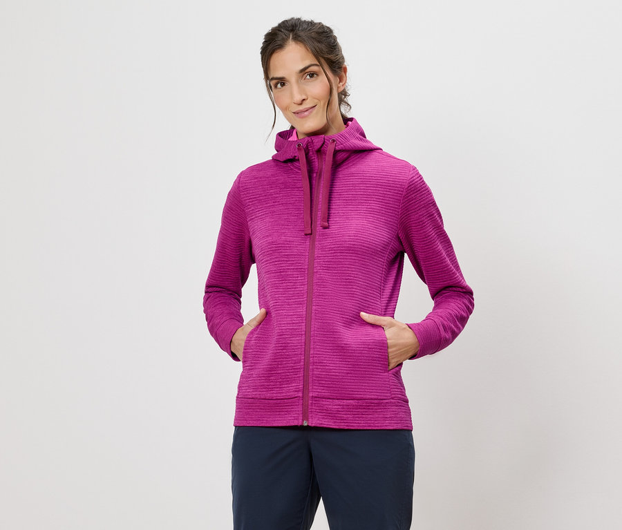 Beyaz bir arka plan önünde elleri ceplerinde pembe kapüşonlu bir kadın.