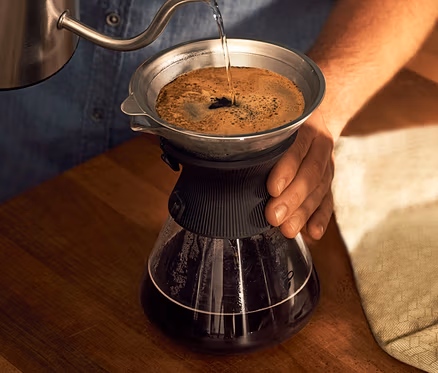 Adam, kahve filtresi olan BEEM Pour Over, 0,75 l cam sürahiye su döküyor.
